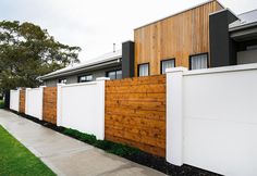 a wooden fence next to a house with white walls and grass in the front yard