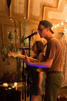 a man playing guitar while standing next to a woman in front of a microphone and other instruments