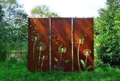 a tall metal screen with flowers on it in the middle of some grass and trees