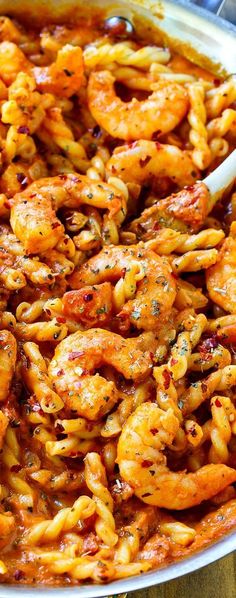 a pan filled with pasta and shrimp on top of a wooden table