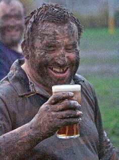 a man covered in mud holding a beer