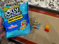 a hand holding a bag of candy next to some candies on a baking sheet