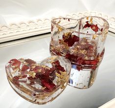 two heart shaped glass containers filled with food on top of a white table next to a mirror