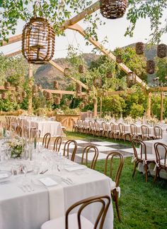 tables and chairs are set up for an outdoor wedding reception with hanging lanterns above them