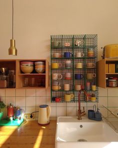 a kitchen area with a sink, counter top and shelves filled with dishes on the wall