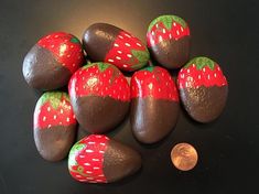 chocolate covered rocks with painted strawberries on them and a penny sitting next to it