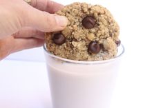 a person holding a cookie in front of a glass of milk with chocolate chips on top