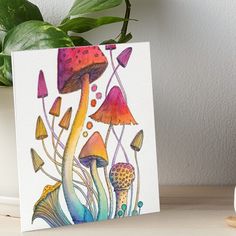 a painting of colorful mushrooms and plants on white paper art board with green plant in the background