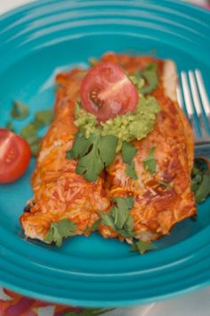 a blue plate topped with an enchilada next to a fork