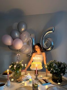 a woman standing in front of a cake with candles on it and balloons behind her