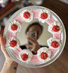 a person holding up a cake with cherries in front of a mirror and taking a selfie