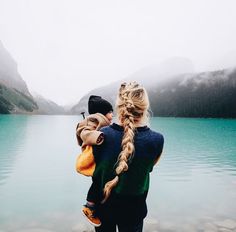 a woman holding a child in her arms while standing next to a body of water