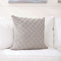 a white couch with a gray pillow on top of it next to a painting hanging on the wall