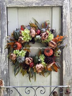 a wreath with flowers and leaves on an old wooden door, hanging from a wrought iron fence