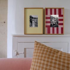 two framed pictures hang on the wall above a pink couch in front of a fireplace