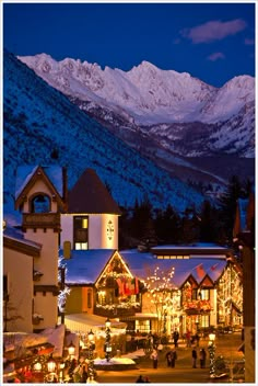 the town is lit up with christmas lights and snow covered mountains in the background at night