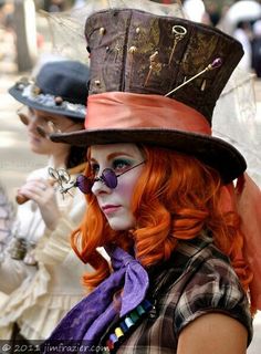 a woman with red hair wearing a top hat and purple scarf on her head while standing next to another woman