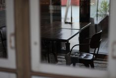 an empty table and chairs are reflected in the glass doors of a restaurant's dining room