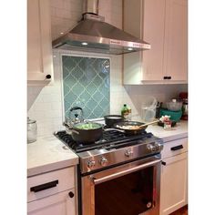 a stove top oven sitting inside of a kitchen next to white cupboards and drawers