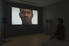 a person sitting in front of a large screen with a man's face on it