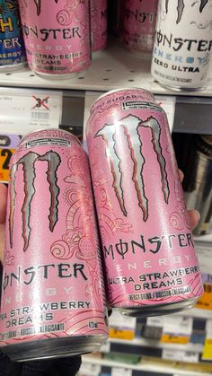 a person holding two cans of monster energy drink in front of the shelves at a store