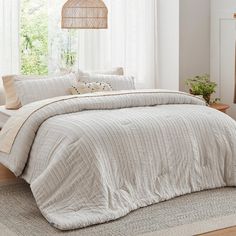 a bed with white linens and pillows in a room next to a window on a rug