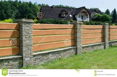 a wooden fence in front of a house with grass and trees on the other side