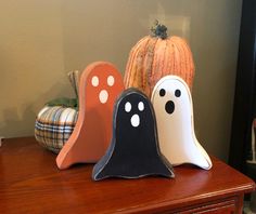 three halloween decorations are sitting on top of a wooden table next to a pumpkin and two ghost heads