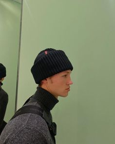 a young man wearing a beanie looking at himself in the mirror