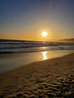 the sun is setting over the ocean with waves coming in from the shore and sand on the beach