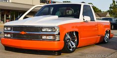 an orange and white truck is parked in front of a store with other cars behind it