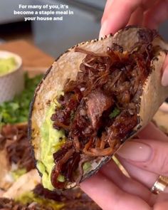 someone is holding up a taco with meat and avocado