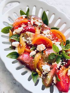 a white plate topped with sliced tomatoes and feta cheese on top of green leaves