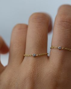 a woman's hand wearing a gold ring with two diamonds on it and a chain around the band