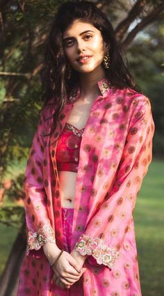 a woman wearing a pink and red outfit standing in front of a tree with her hands on her hips