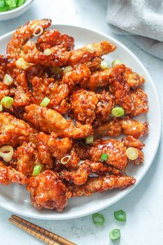 chicken wings with sesame seeds and green onions on a white plate next to chopsticks