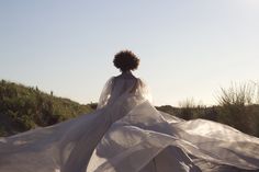 a woman in a white dress is standing on the sand with her back to the camera