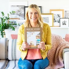 a woman sitting on a couch holding up a house story book in front of her face