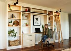 a woman sitting on a chair in front of a desk with shelves and ladders