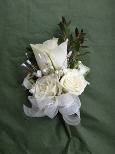 a bouquet of white roses and greenery on a green cloth with ribbon around it