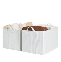 two large white storage baskets with handles on each side and pillows in the bottom one