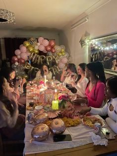 a group of people sitting around a table with food and balloons in the background at a party