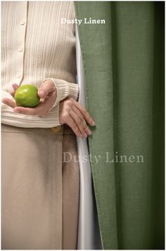 a woman is holding an apple in her hand while standing next to a green curtain