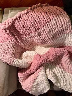 a pink and white crocheted blanket laying on top of a bed next to a pillow