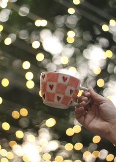 a hand holding a cup with hearts on it in front of boket lights