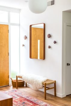 a room with a bench, mirror and rug on the floor in front of it