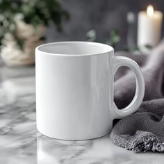 a white coffee mug sitting on top of a counter next to a candle and towel