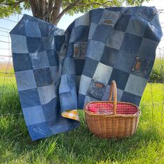 two blankets and a basket sitting in the grass next to a fence with a tree