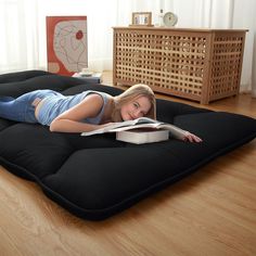 a woman laying on top of an inflatable mattress reading a book while lying on the floor