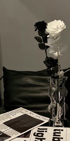 a white rose in a clear vase on a black leather couch with newspapers and magazines